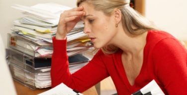 Female office worker sitting at desk with paperwork piled high